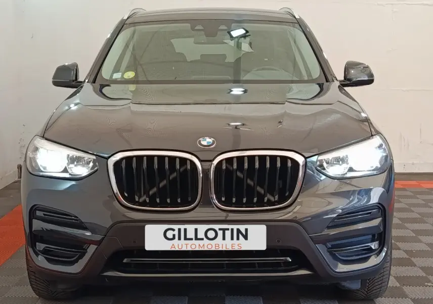 Vue avant d'un BMW X3 gris clair avec calandre double haricot et phares LED allumés en intérieur showroom.