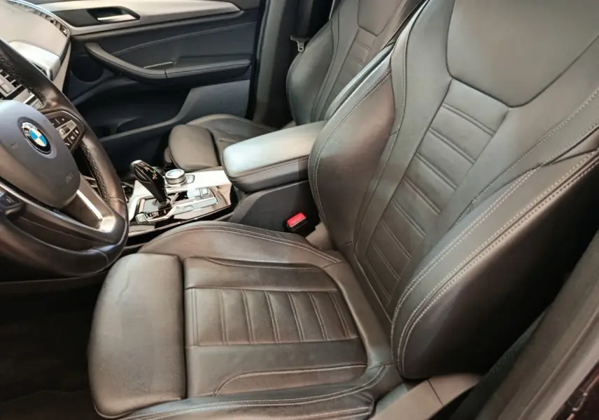 Vue intérieure côté conducteur d'une BMW X3 2020, sièges cuir noirs et volant multifonctions alu et cuir.