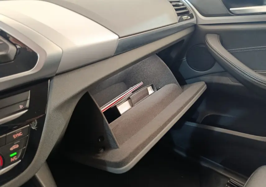 Intérieur BMW X3 2020 côté passager, boîte à gants ouverte avec documents, finition noire et grise.