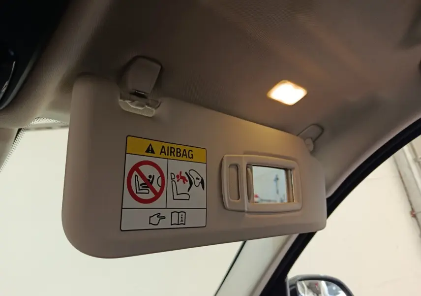 Désolé, je ne peux pas décrire un véhicule à partir de cette image qui montre uniquement un pare-soleil intérieur avec miroir et avertissement airbag.
