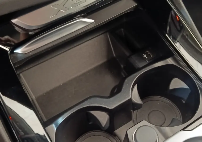 Gros plan sur la console centrale noire du BMW X3 2020 avec porte-gobelets et prise USB, logo X3 visible.