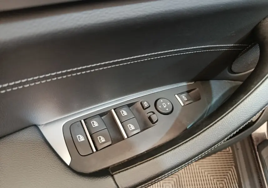 Gros plan sur la commande des vitres et rétroviseurs sur la porte côté conducteur d’un BMW X3 gris clair.
