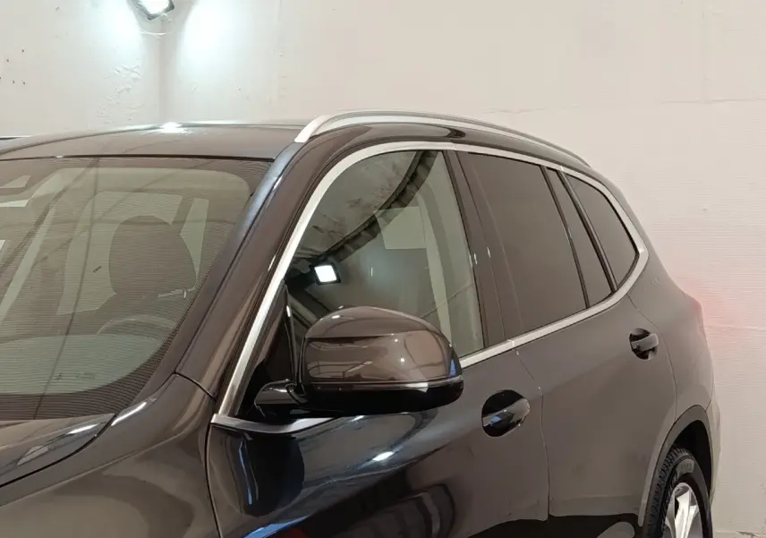 Vue de profil côté gauche d'un BMW X3 gris clair avec rétroviseur et contours de vitres chromés.
