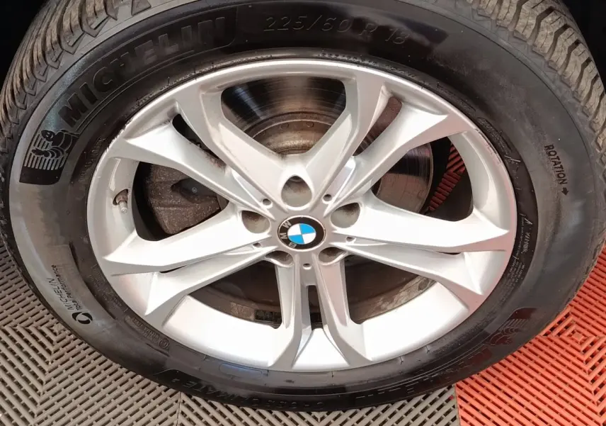 Gros plan sur la jante alu argentée avec logo BMW au centre et pneu Michelin noir.