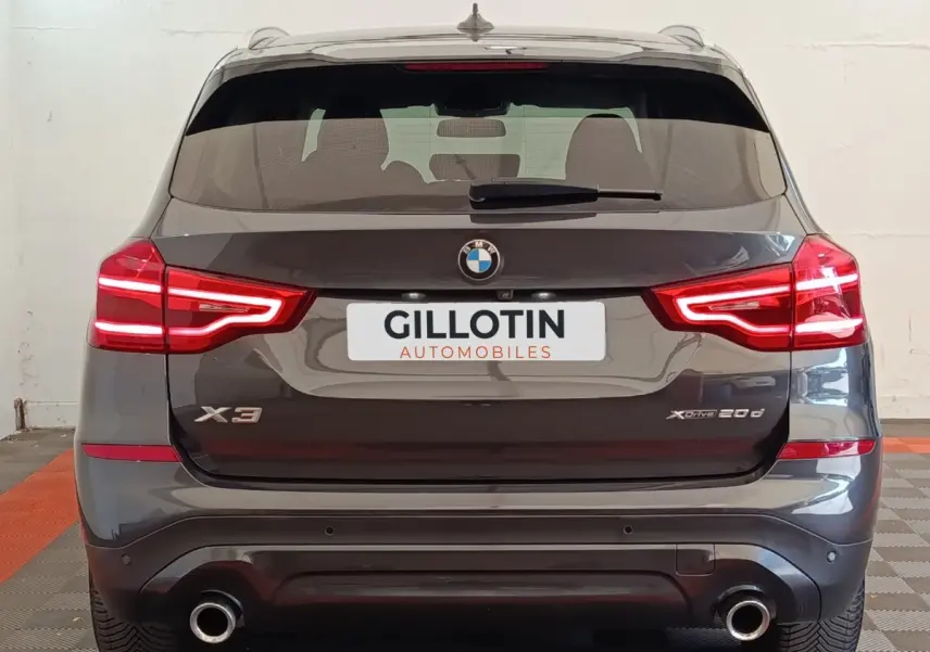 Vue arrière d’un BMW X3 gris clair 2020 avec feux LED allumés et double sortie d’échappement visible.