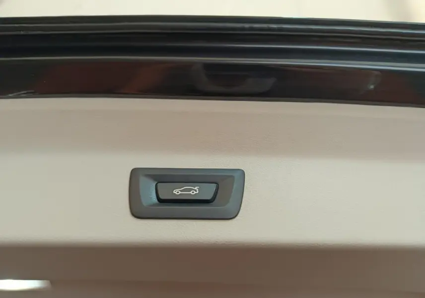 Bouton d'ouverture électrique du coffre sur la garniture intérieure beige d'un BMW X3 gris clair.