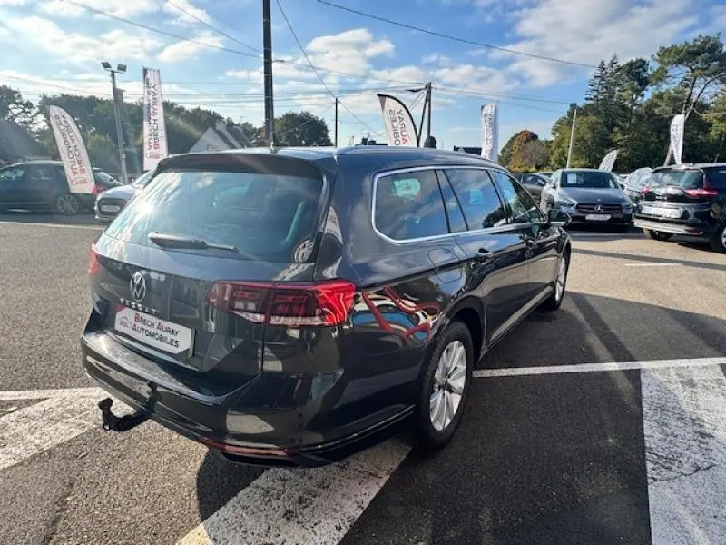 Volkswagen Passat SW gris manganèse métallisé vue 3/4 arrière droit avec attelage et barres de toit visibles.