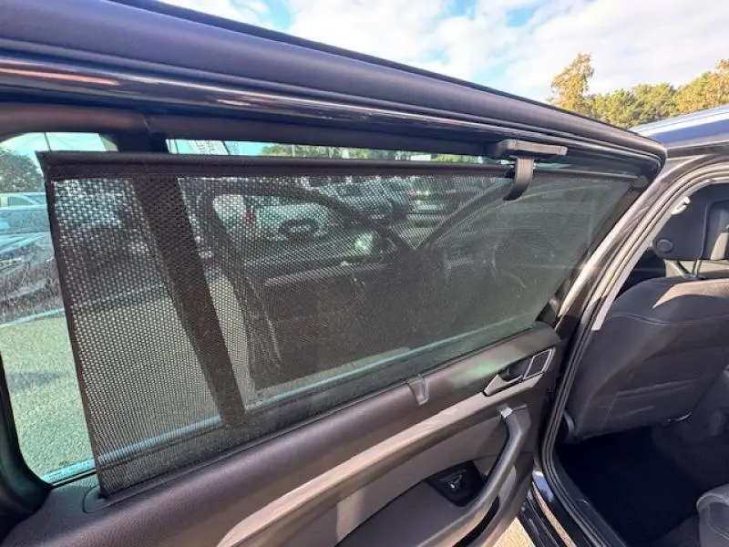 Vue intérieure côté gauche de la Volkswagen Passat SW 2022 gris manganèse, avec store pare-soleil déployé sur la porte arrière.