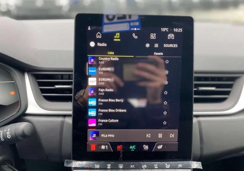 Vue rapprochée de l’écran tactile central du Renault Captur 2025 affichant la liste des radios avec commandes climatisation en dessous.