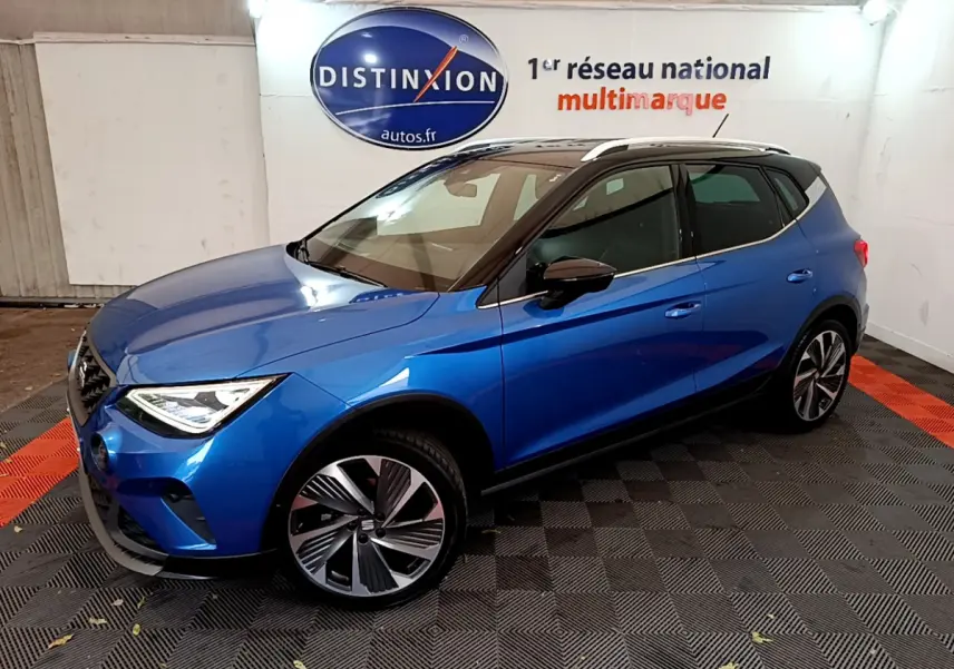 Vue 3/4 avant droite d’un SEAT Arona bleu 2022 avec toit noir et jantes alliage distinctives dans un showroom.
