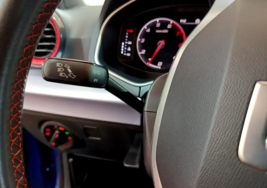 Gros plan sur le volant et le combiné d'instruments digital du SEAT Arona bleu, avec détails du commodo et coutures rouges.