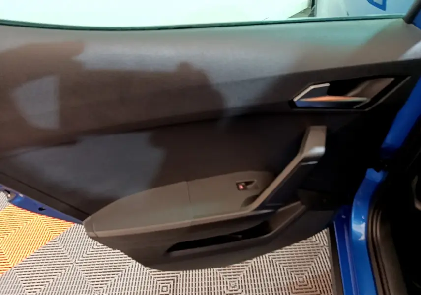 Vue intérieure côté gauche de la porte avant bleue du SEAT Arona 2022, avec poignée et commande de lève-vitre.