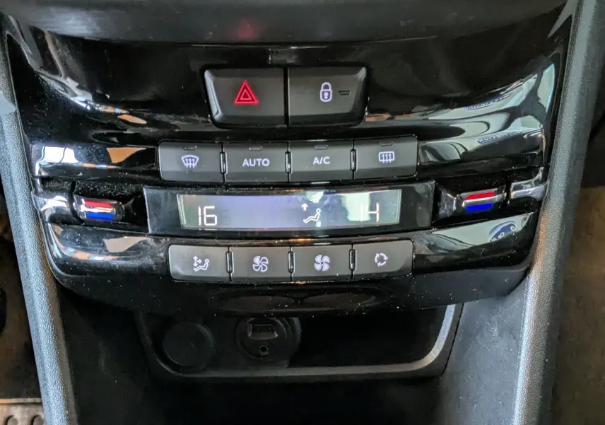 Gros plan sur la console centrale noire du Peugeot 2008 blanche, montrant les commandes de climatisation digitale et boutons de sécurité.