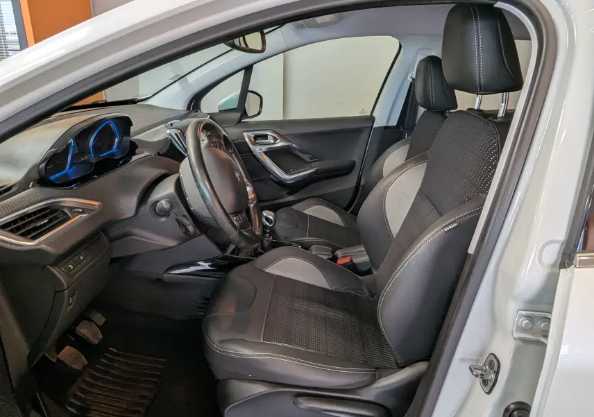 Vue intérieure côté conducteur de la Peugeot 2008 blanche, mettant en valeur les sièges noirs et gris et le tableau de bord moderne.
