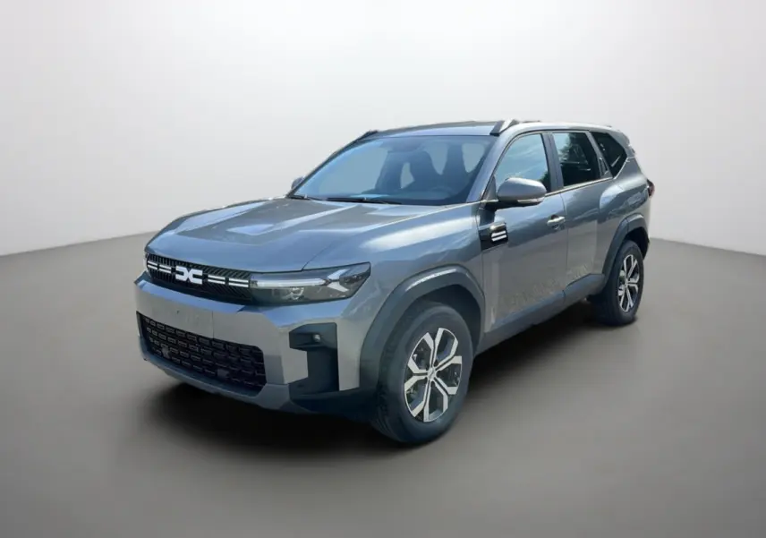 Vue 3/4 avant du Dacia Bigster gris schiste avec jantes alu 17 pouces et barres de toit visibles.