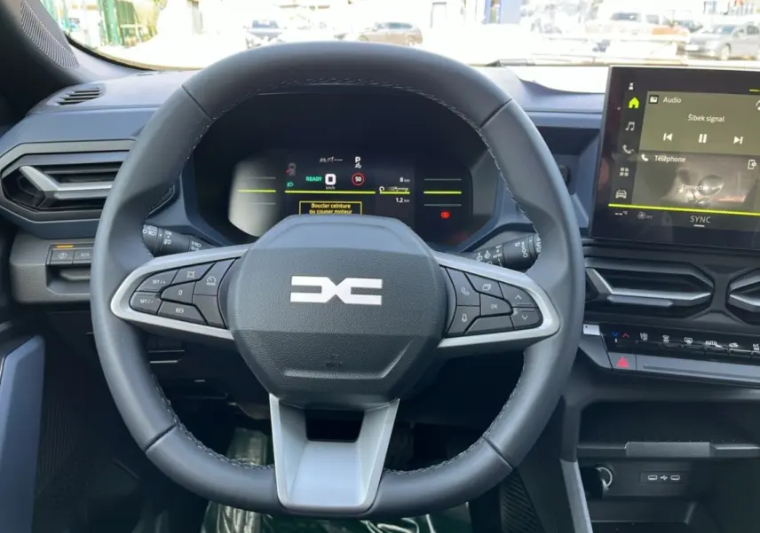 Vue rapprochée du volant cuir noir du Dacia Bigster Hybrid 155 Expression Plus avec tableau de bord digital et écran tactile.