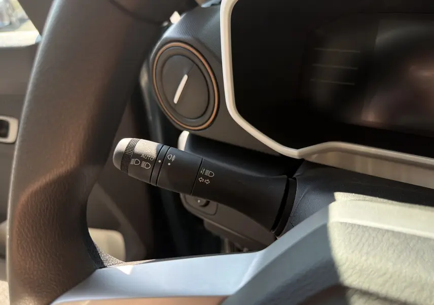 Gros plan sur la manette de commandes d'éclairage à gauche du volant dans le tableau de bord du Dacia Spring 65 Extreme bleu ardoise 2026.