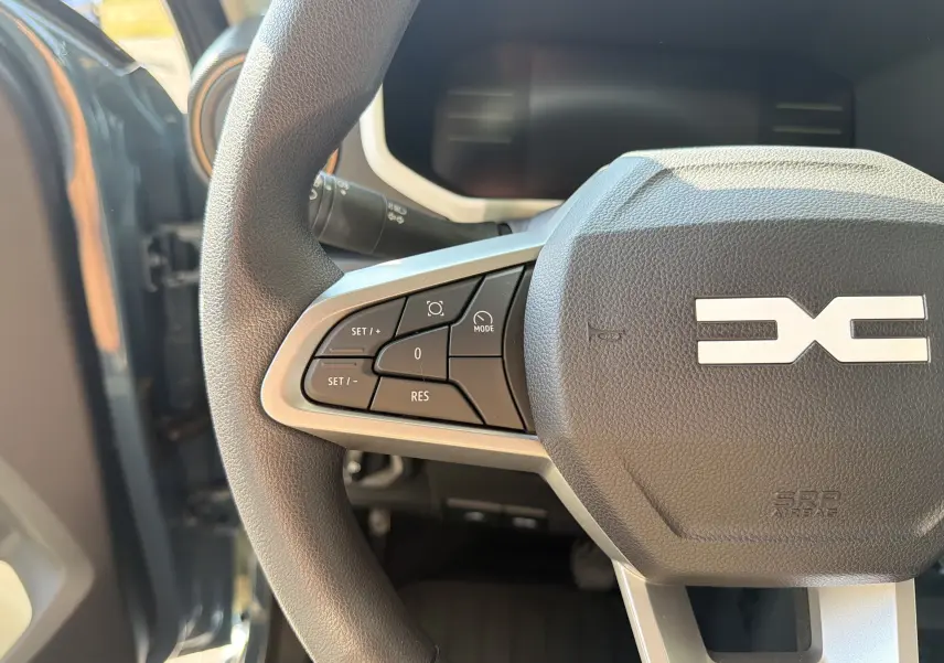 Gros plan sur le volant du Dacia Spring 65 Extreme 2026, montrant les commandes à gauche et le logo central en relief.