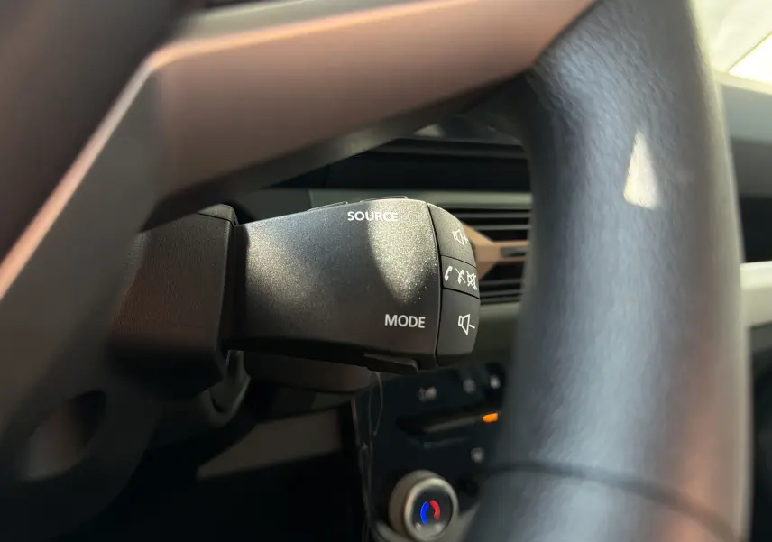Gros plan sur la commande au volant du DACIA Spring 65 Extreme 2026, avec boutons source et mode visibles, intérieur noir.