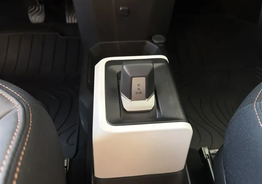 Gros plan sur le levier de vitesses automatique noir et gris dans l’habitacle du Dacia Spring 65 Extreme 2026, sièges avec surpiqûres orange visibles.