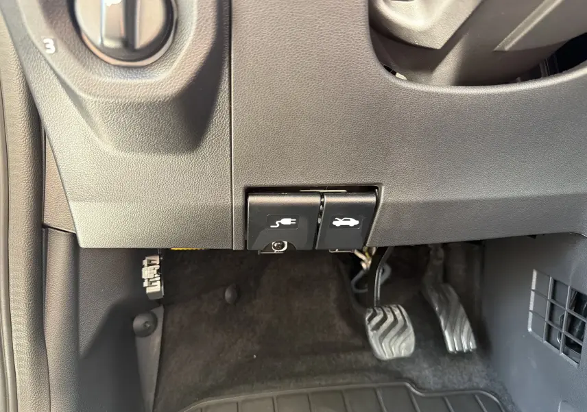 Gros plan sur les commandes d'ouverture du capot et de la trappe de recharge électrique sous le tableau de bord d'une Dacia Spring 65 Extreme 2026.