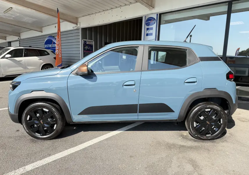 Vue de profil côté gauche d'une Dacia Spring 65 Extreme 2026 bleu ardoise avec jantes noires et protections latérales noires.