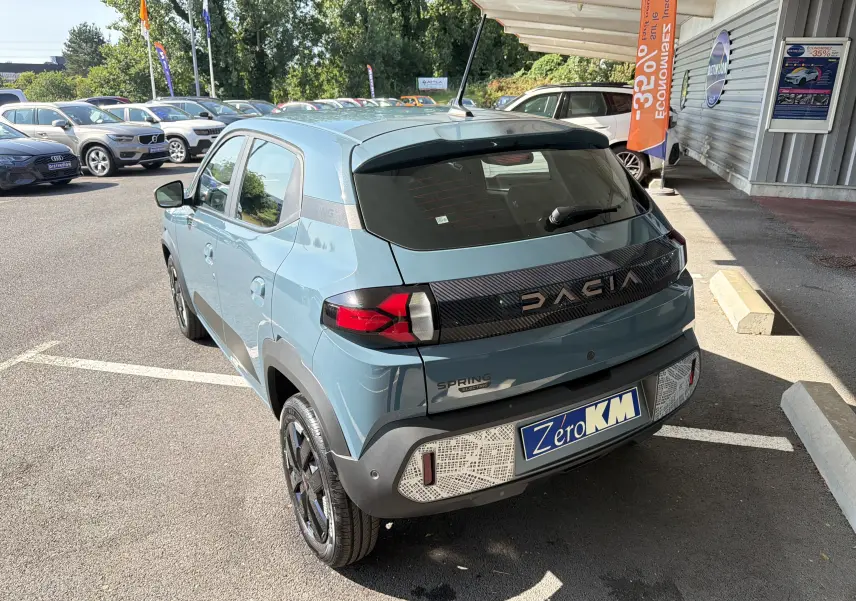 Vue 3/4 arrière d'une Dacia Spring 65 Extreme électrique bleu ardoise avec détails noirs et logo DACIA lumineux.
