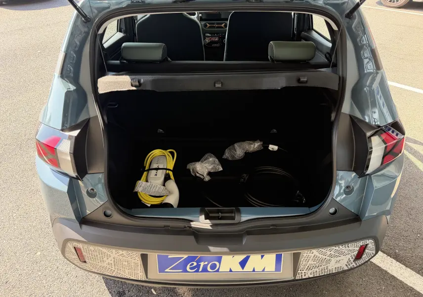 Coffre ouvert vu de l'arrière d'une Dacia Spring 65 Extreme bleu ardoise 2026 avec câbles de recharge visibles.