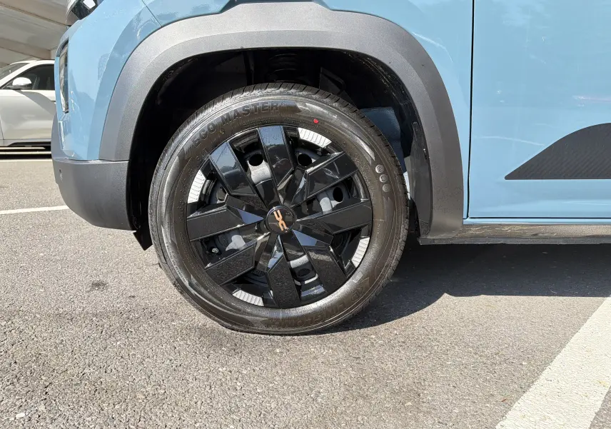 Gros plan sur la roue avant gauche du Dacia Spring 65 Extreme 2026 bleu ardoise, avec jante noire et détails blancs.