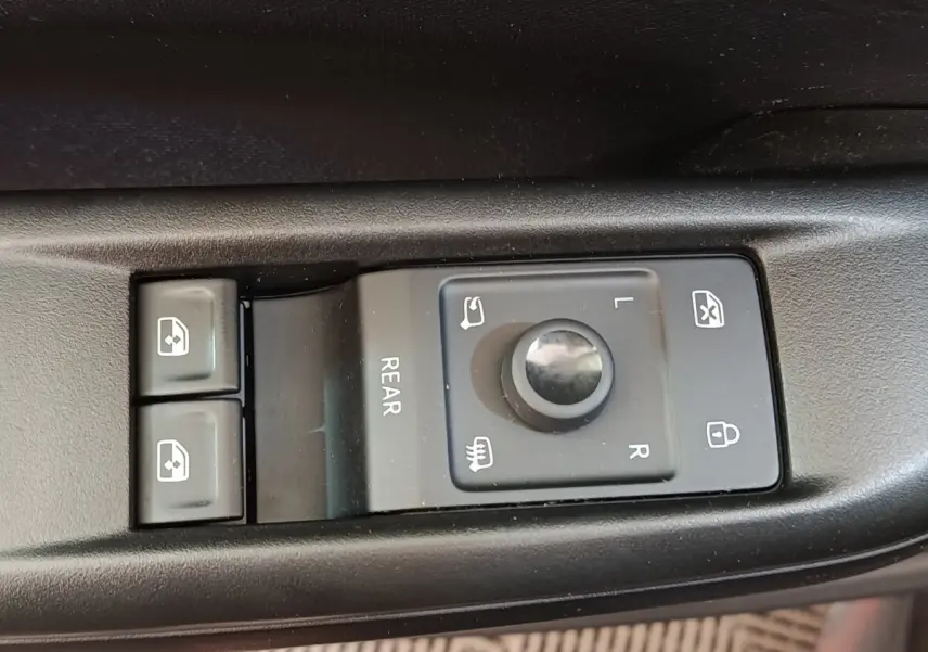 Gros plan sur les commandes de réglage des rétroviseurs et des vitres électriques côté conducteur d'une CUPRA Born gris foncé.