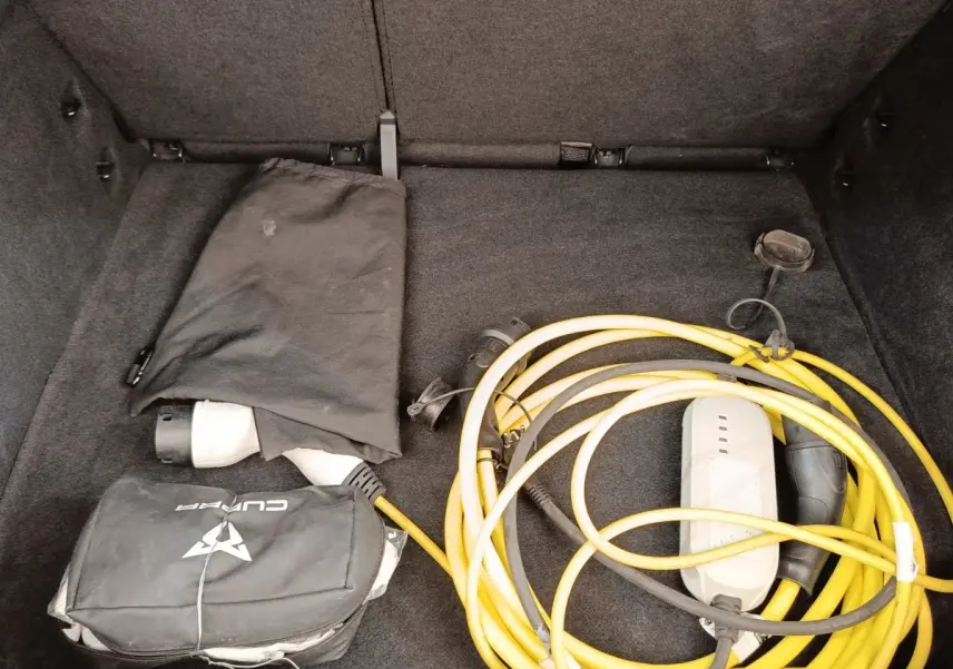 Coffre ouvert d’une CUPRA BORN gris foncé, montrant un câble de recharge électrique jaune enroulé et une housse noire.