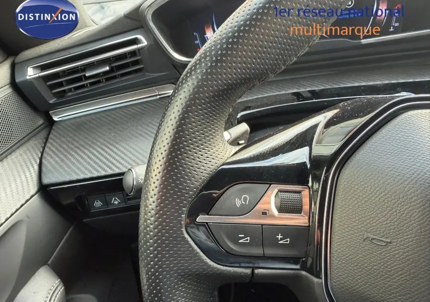 Gros plan sur le volant en cuir perforé côté gauche du Peugeot 508 gris platinium avec commandes audio intégrées.