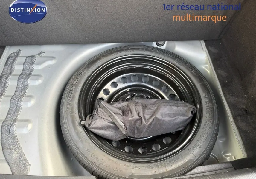 Roue de secours noire dans le coffre d'une Peugeot 508 gris platinium, vue plongeante sur le pneu et son sac d'outils.