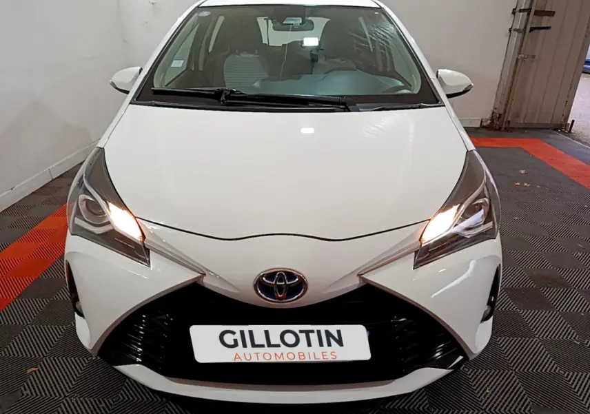Vue avant d'une Toyota Yaris blanche 2020 avec phares allumés et calandre noire distinctive.