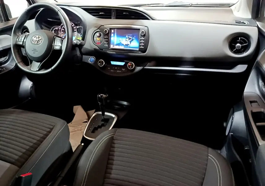 Vue intérieure avant de la Toyota Yaris 1.5 Hybride 2020, tableau de bord avec écran tactile et volant multifonctions noir.