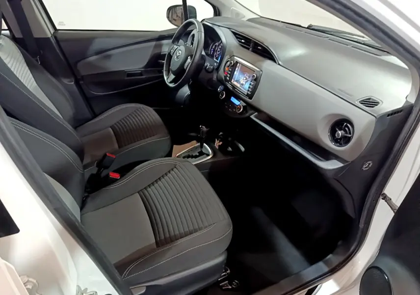 Vue intérieure côté conducteur de la Toyota Yaris blanche 2020, montrant sièges noirs et tableau de bord avec écran tactile.