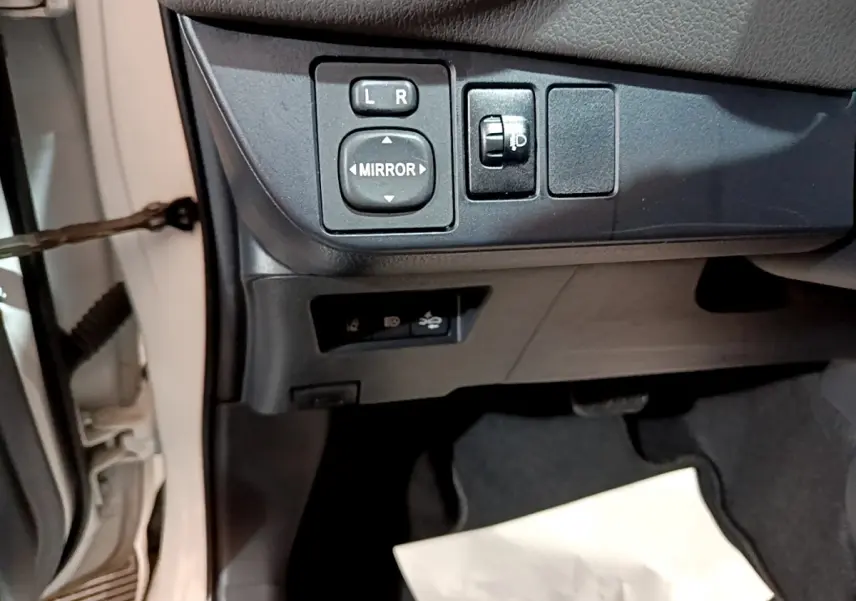 Vue intérieure côté gauche de la Toyota Yaris blanche, montrant les commandes de réglage des rétroviseurs et des phares.