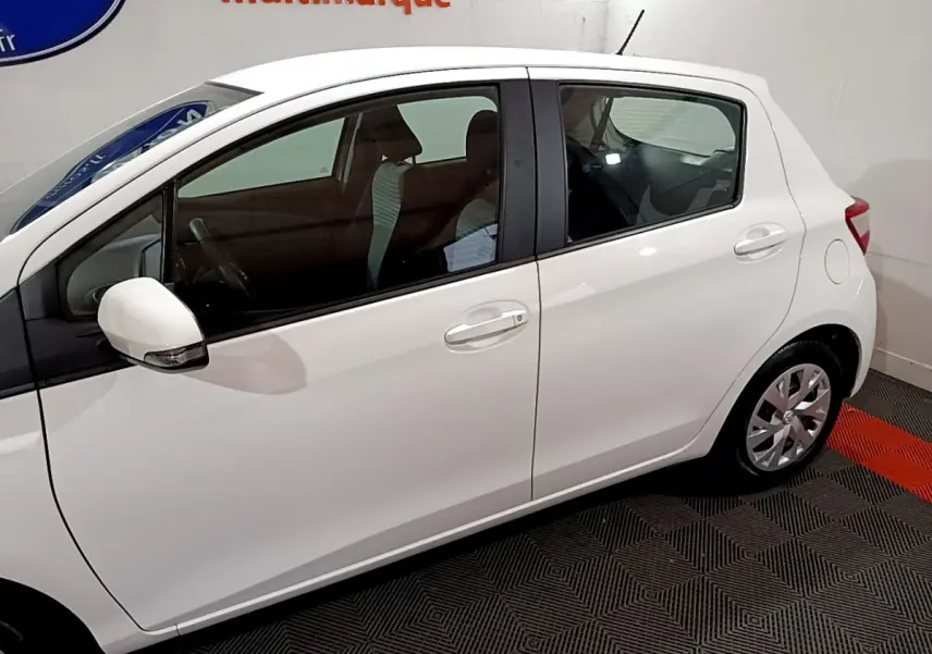 Vue de profil côté gauche d'une Toyota Yaris blanche 2020, version hybride, en intérieur sur sol à damier noir et rouge.
