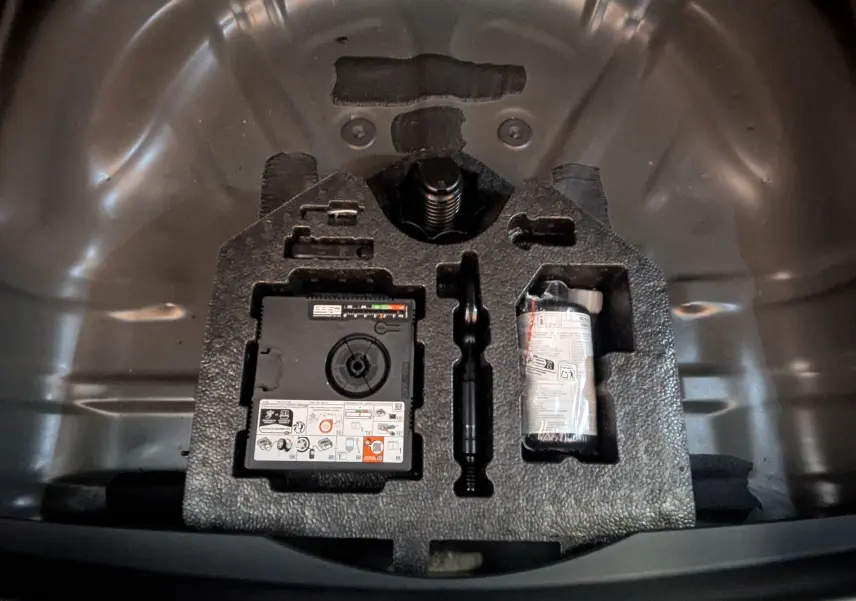 Gros plan sur le compartiment de rangement sous le coffre du CUPRA Formentor noir 2025, montrant l’équipement de secours.