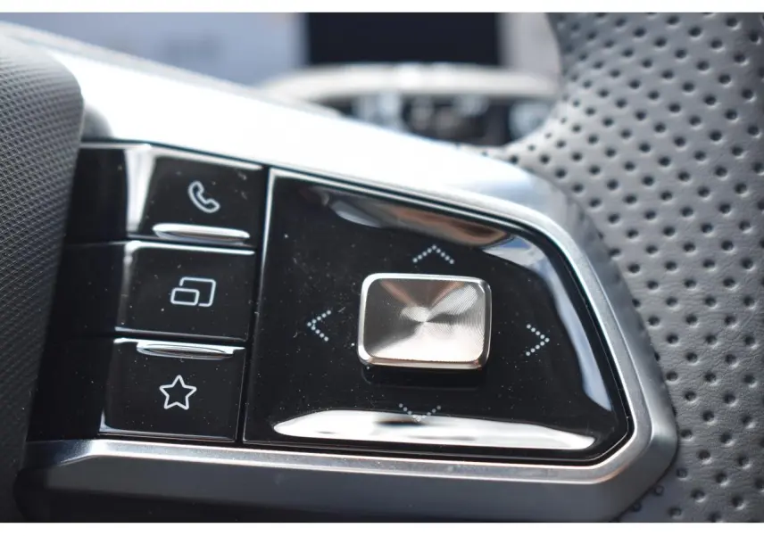 Gros plan sur les commandes multifonctions en plastique noir et chrome du volant perforé du MG Motor EHS gris.