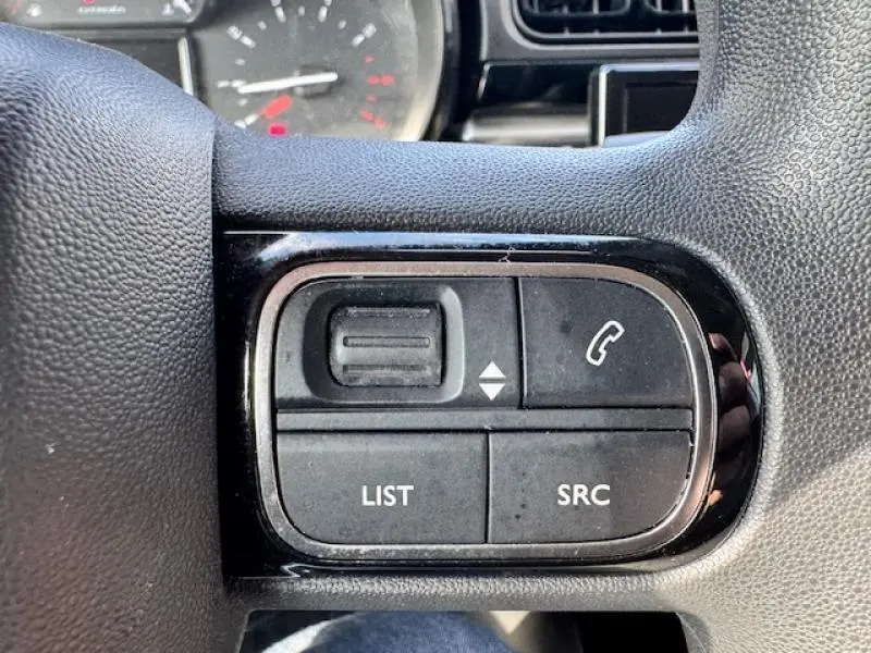 Gros plan sur les commandes audio et téléphone intégrées au volant cuir de la Citroën C3 blanche de 2021.