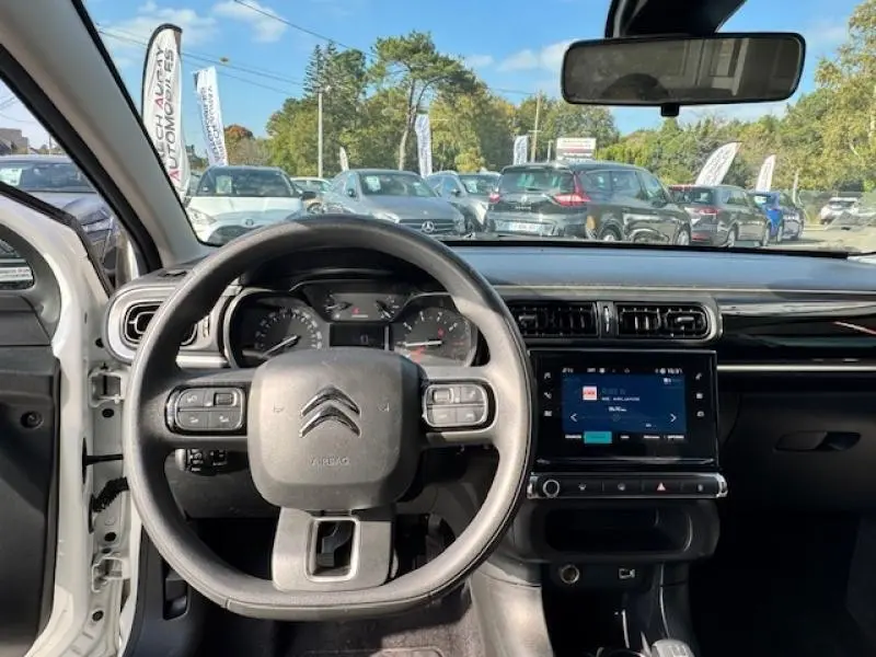 Vue intérieure frontale du tableau de bord et volant cuir noir d'une Citroën C3 1.2 essence blanche avec écran tactile allumé.