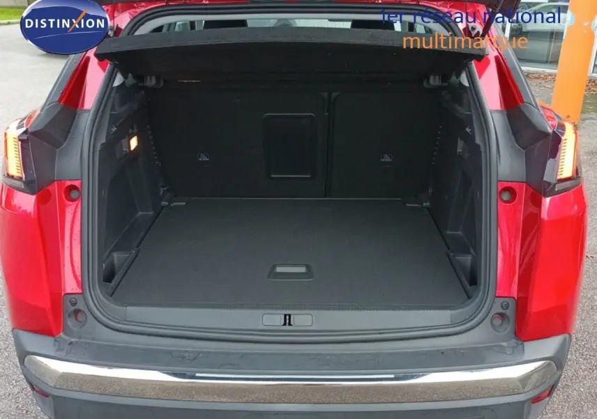 Coffre ouvert d'un Peugeot 3008 rouge foncé métal vu de l'arrière, montrant l'espace de chargement vide et les feux arrière allumés.