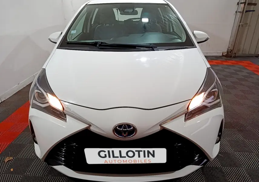 Vue avant d'une Toyota Yaris blanche 2019 avec phares allumés et calandre noire distinctive.