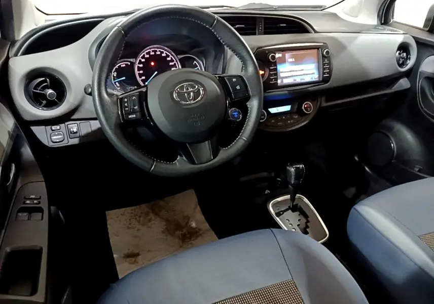 Vue intérieure avant de la Toyota Yaris blanche, volant cuir alu multifonctions et écran tactile central visible.