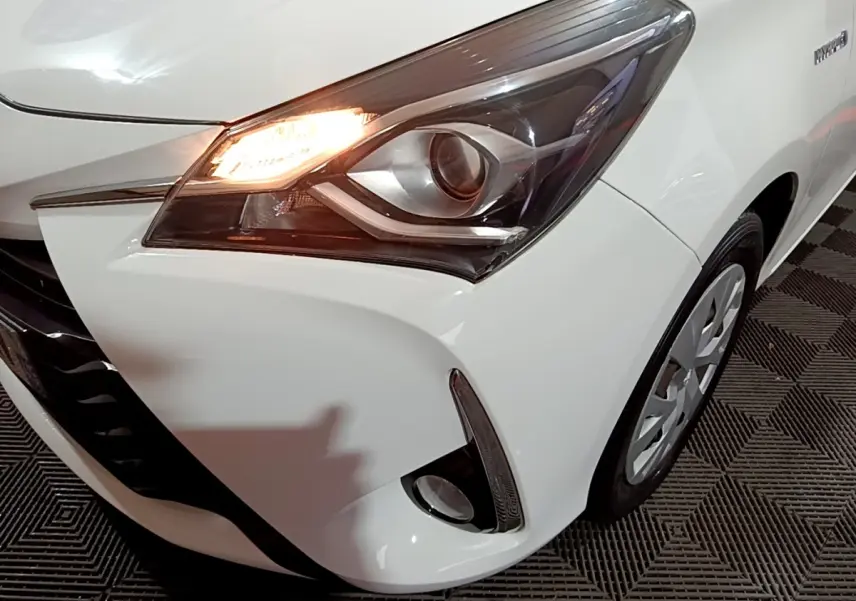 Gros plan sur l'avant droit blanc de la Toyota Yaris hybride 2019 avec phare allumé et antibrouillard visible.