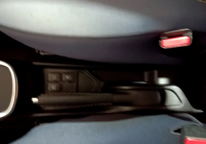 Vue rapprochée de la console centrale de la Toyota Yaris blanche, montrant le frein à main et les boutons de commande.