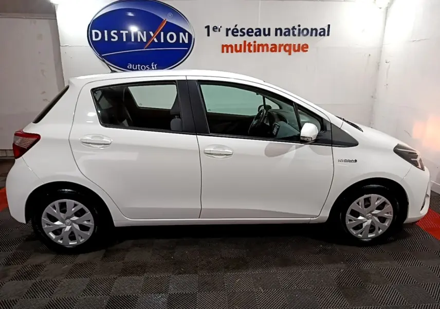 Vue de profil côté gauche d'une Toyota Yaris blanche hybride 2019, avec jantes et rétroviseurs blancs dans un showroom.