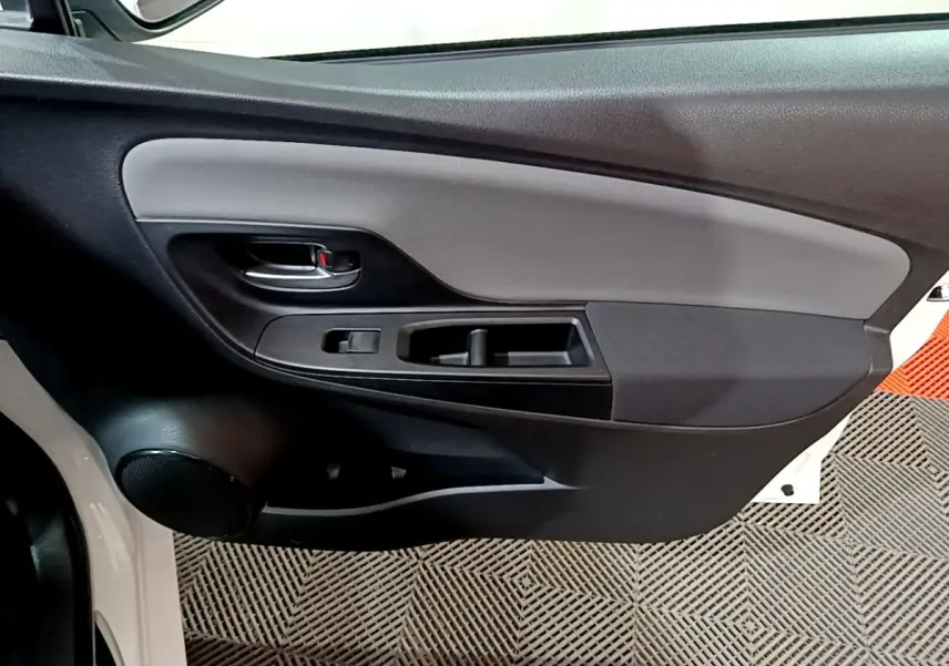 Vue rapprochée de la porte avant gauche de la Toyota Yaris blanche, montrant la poignée intérieure et les commandes de fenêtre.