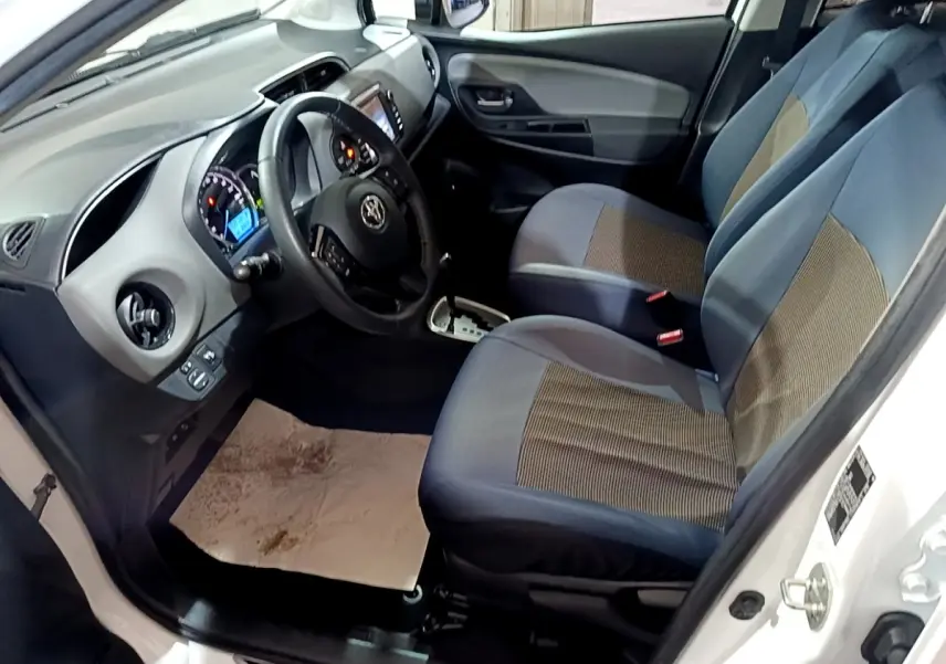 Vue intérieure côté conducteur d'une Toyota Yaris blanche 2019, volant cuir alu multifonctions et sièges tissu bicolore.